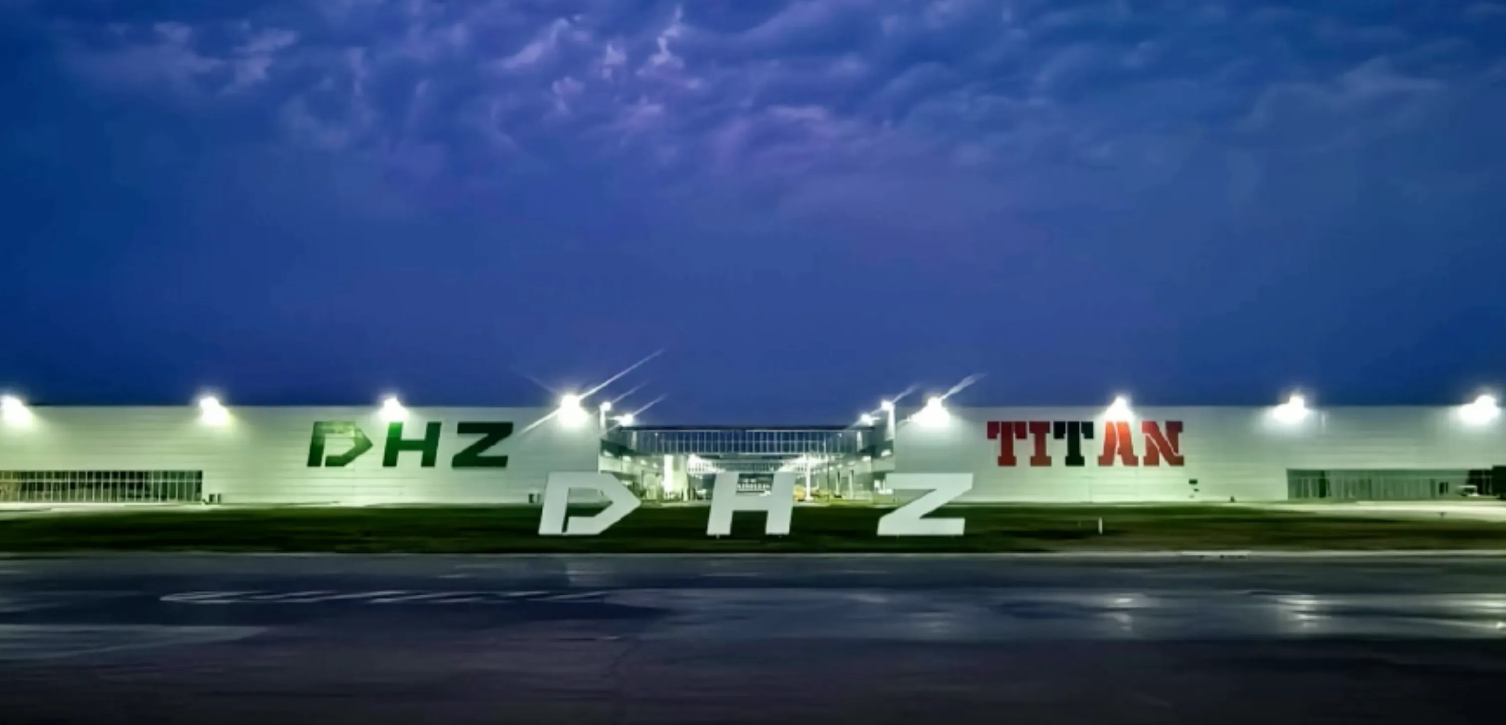 Produktionswerk von DHZ Fitness bei Nacht, beleuchtete Werkhalle mit großem DHZ-Schriftzug